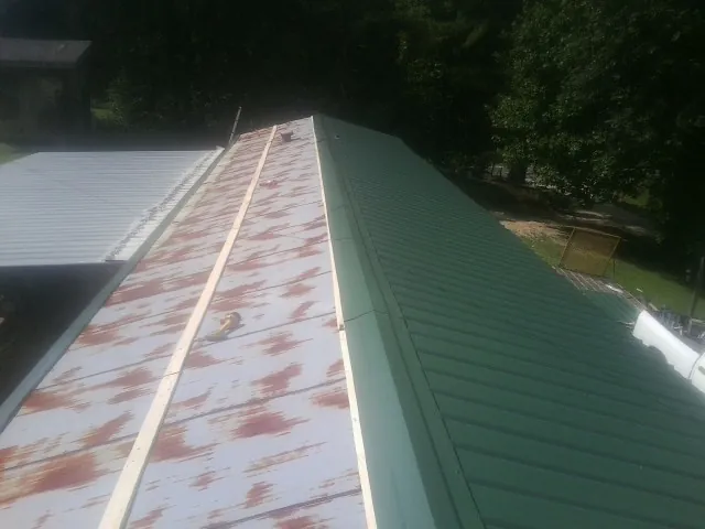 Old rusted panels beside newly installed green metal roofing — Wind Damage Roof Repair by Roofing Brothers in Spring Lake